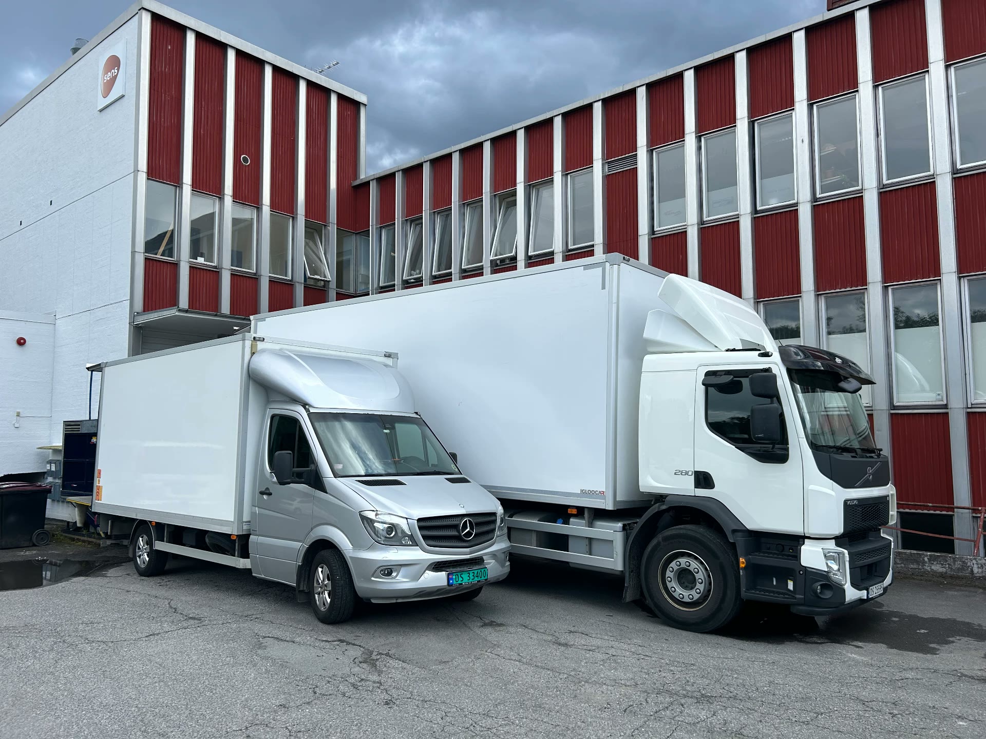 To hvite flyttebiler parkert foran næringsbygg