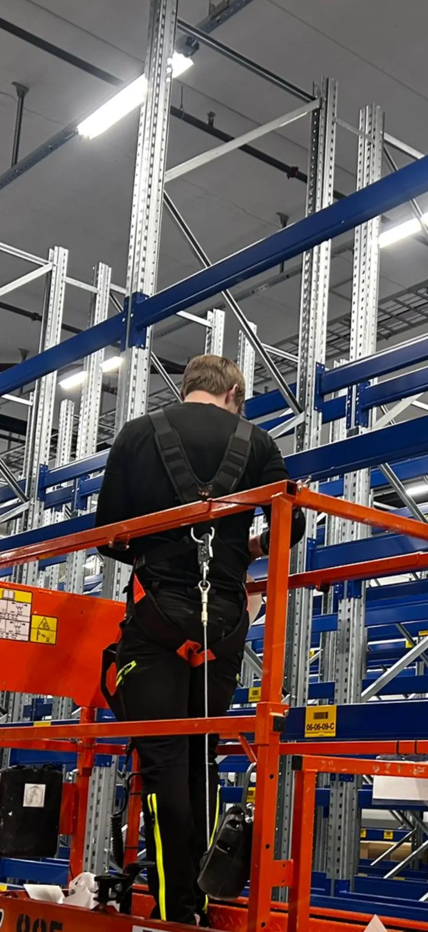 Montør i sikkerhetssele monterer lagerreoler fra lift